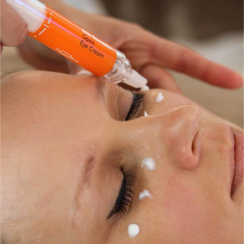 A skincare professional applying eye cream to clients eyelids with a small applicator.